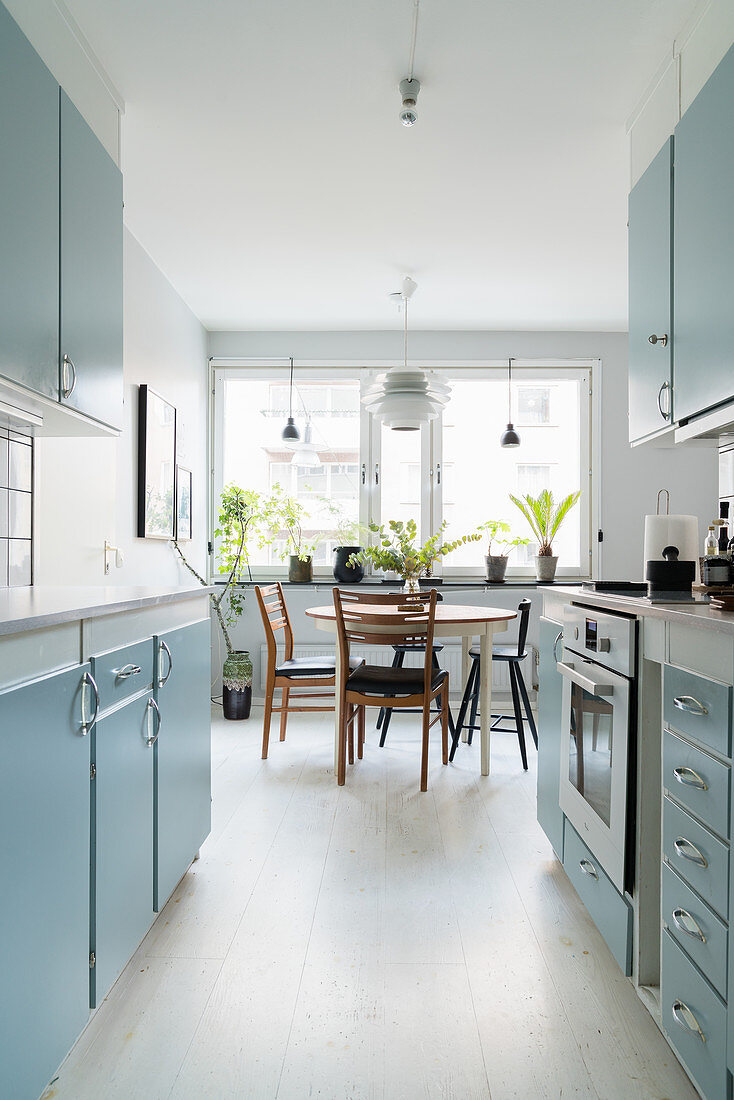 Retro-Küche mit hellblauen Fronten und Esstisch vor dem Fenster