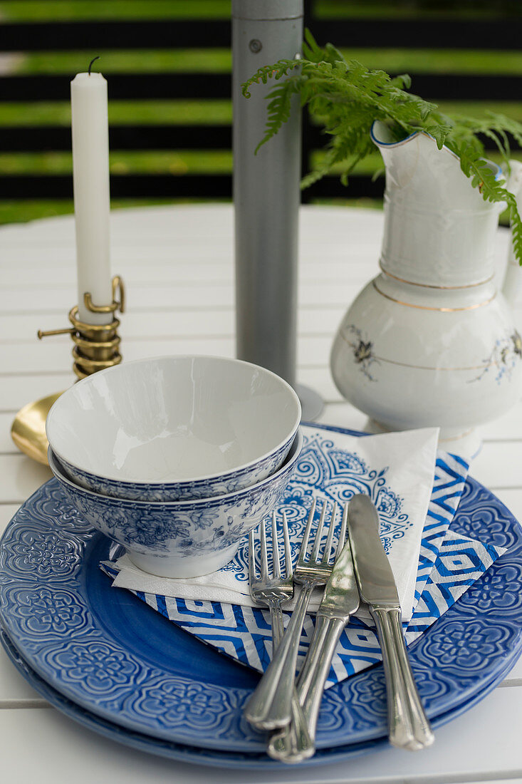 Blau-weißes Gedeck, Kerze und Krug auf Gartentisch