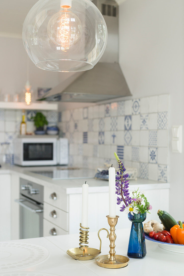 Candles and vase of flowers on dining table below spherical glass lamp in open-plan kitchen