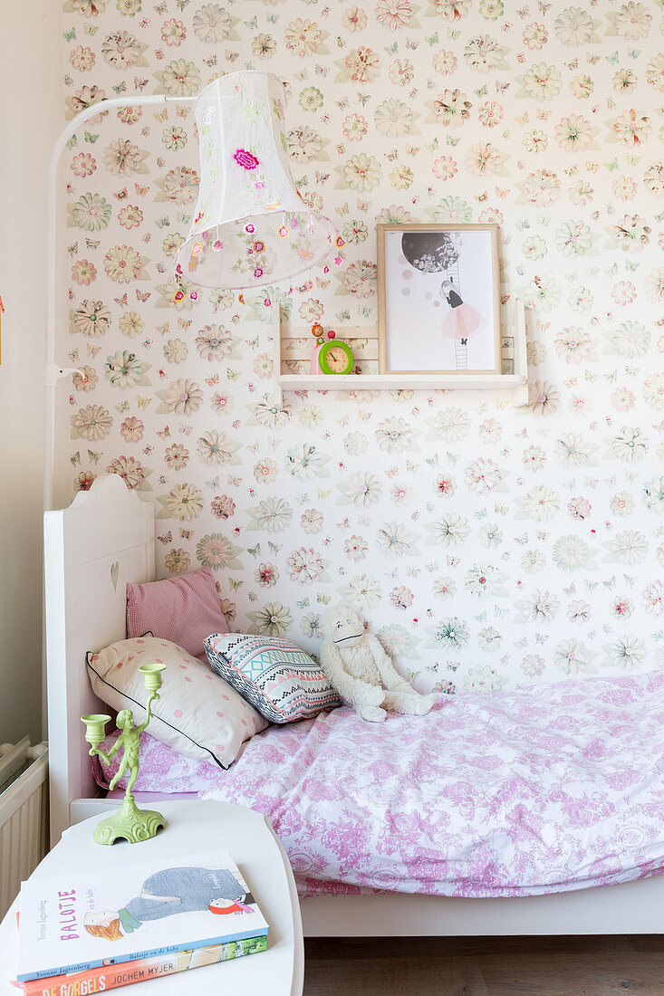 Bed against floral wallpaper in vintage-style child's bedroom