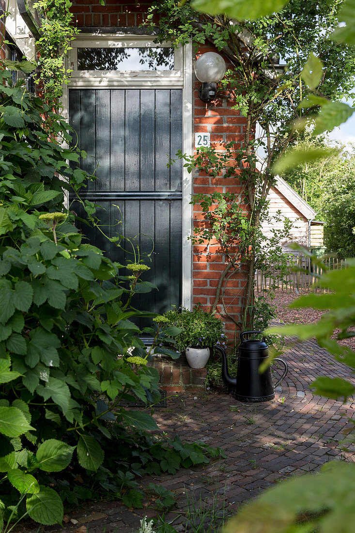 Weg aus Backsteinen an einem bewachsenen Haus mit Gartentür