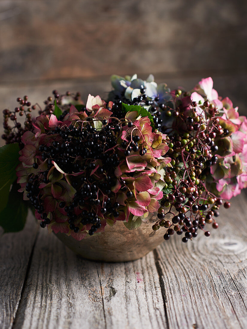 Holunderbeeren und Hortensienblüten in Vase auf Holztisch