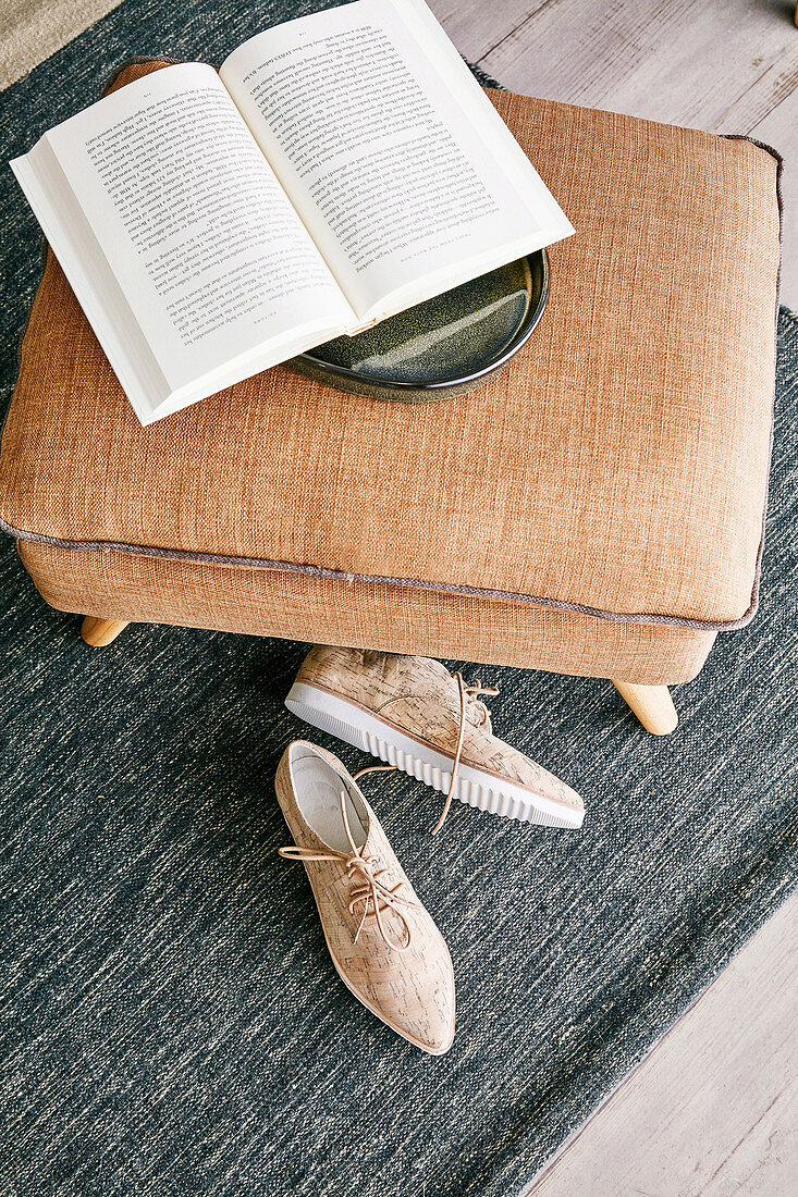 Open book on brown ottoman and beige shoes
