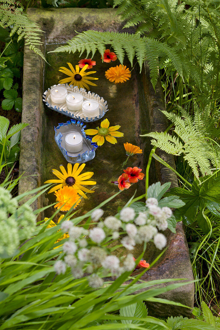 DIY Schwimmlichter aus Fischdosen mit Fransen und Blüten in einem Sandsteintrog