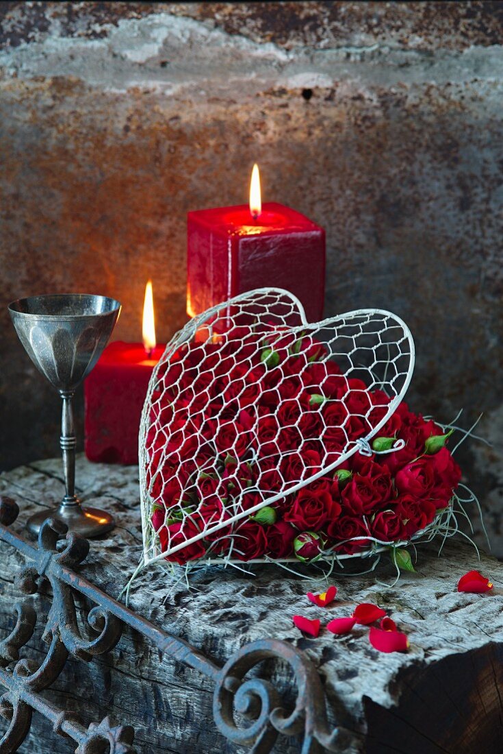 Red roses in wire love heart in front of red pillar candles