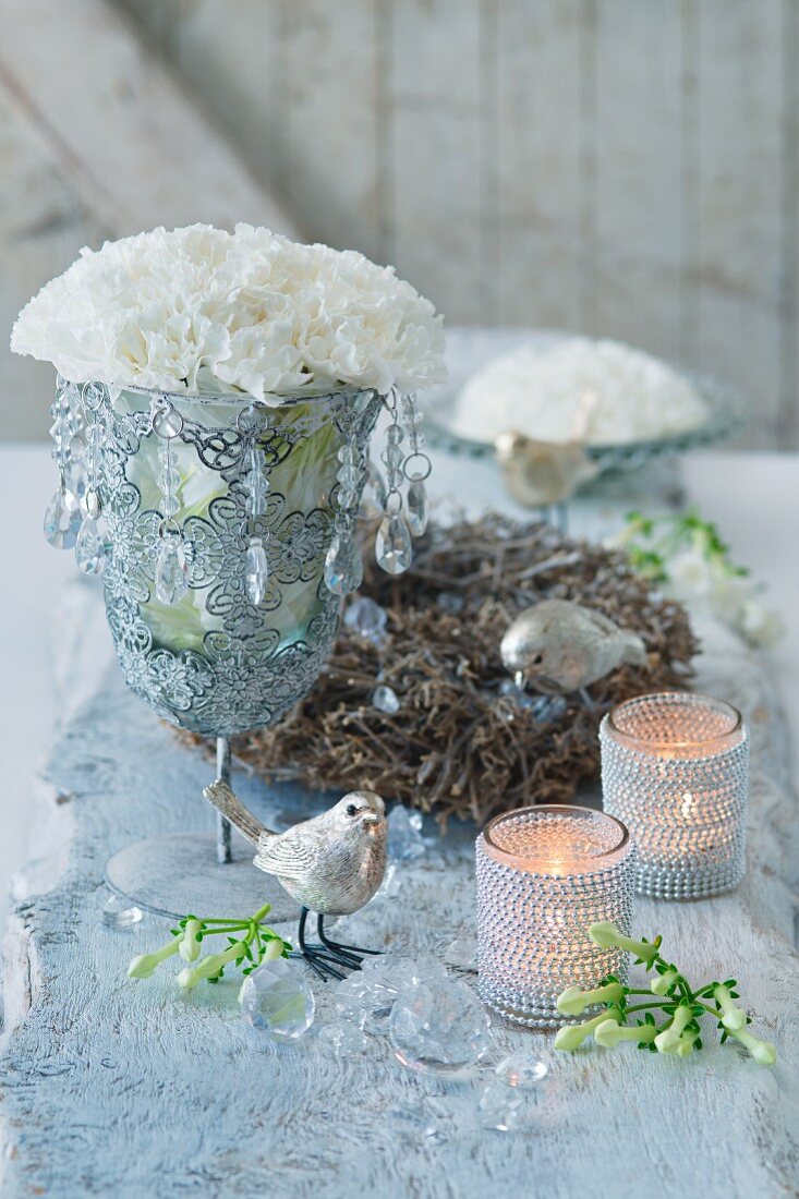 White carnations in goblet with crystal droplets, bird ornaments and tealight holders