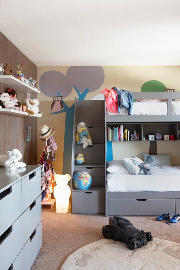Loft bed with drawers below against mural on wall in child's bedroom