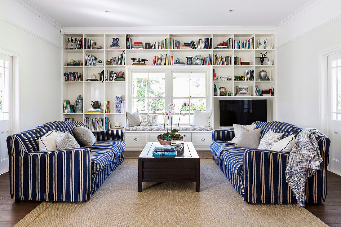 Zwei gegenüberstehende blau-weiß gestreifte Sofas vor einer Regalwand
