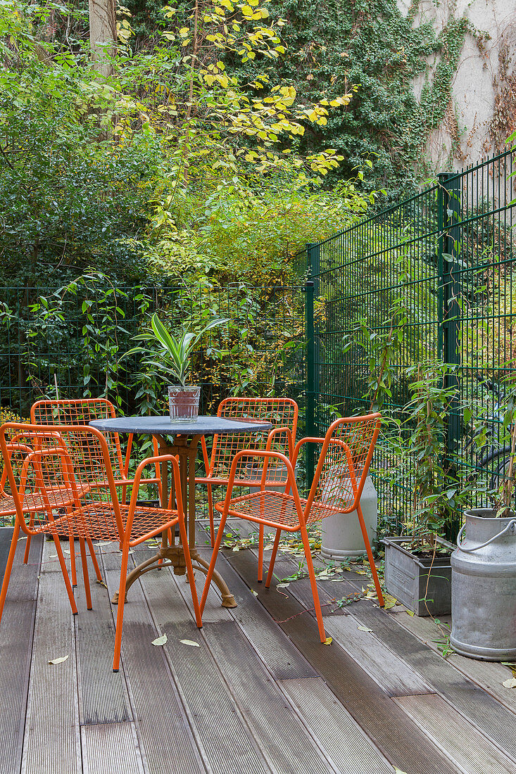 Orangefarbene Metallstühle und Tisch auf Holzterrasse