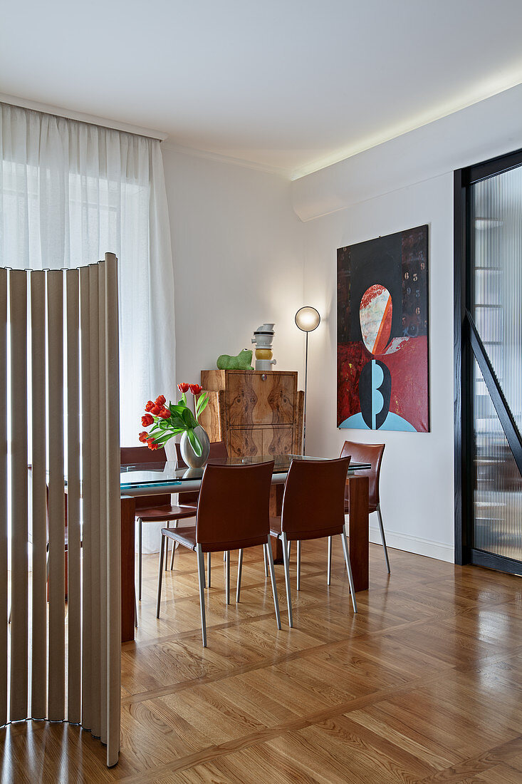 Elegant dining table and chairs in front of painting in open-plan interior divided by screen made from cardboard tubes