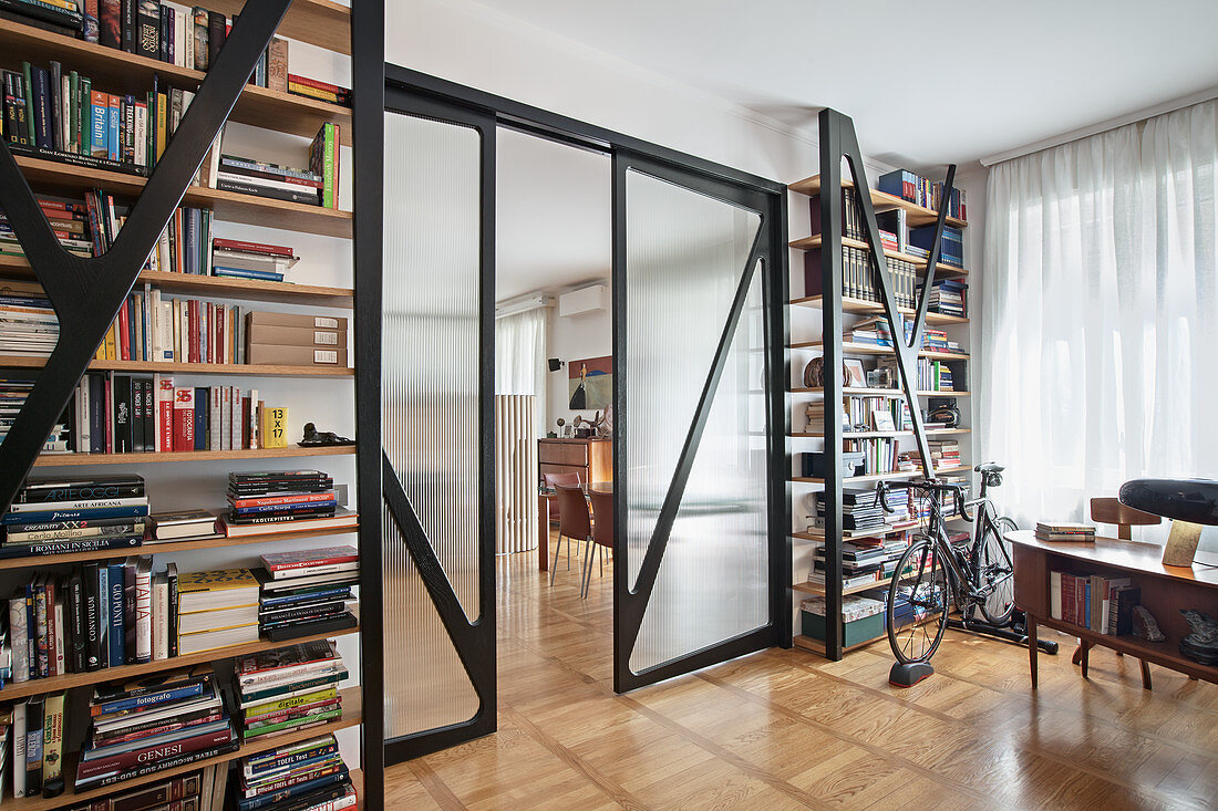 Arbeitszimmer mit raumhohen Bücherregalen und Glasschiebetüren, Fahrrad vor dem Fenster