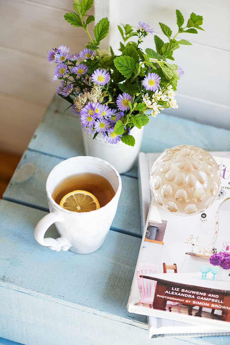 Eine Tasse Tee, Blumen und Glaskugel auf Buch