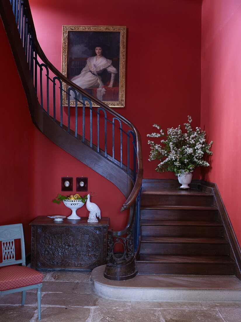 Old trunk below curved wooden staircase with red walls
