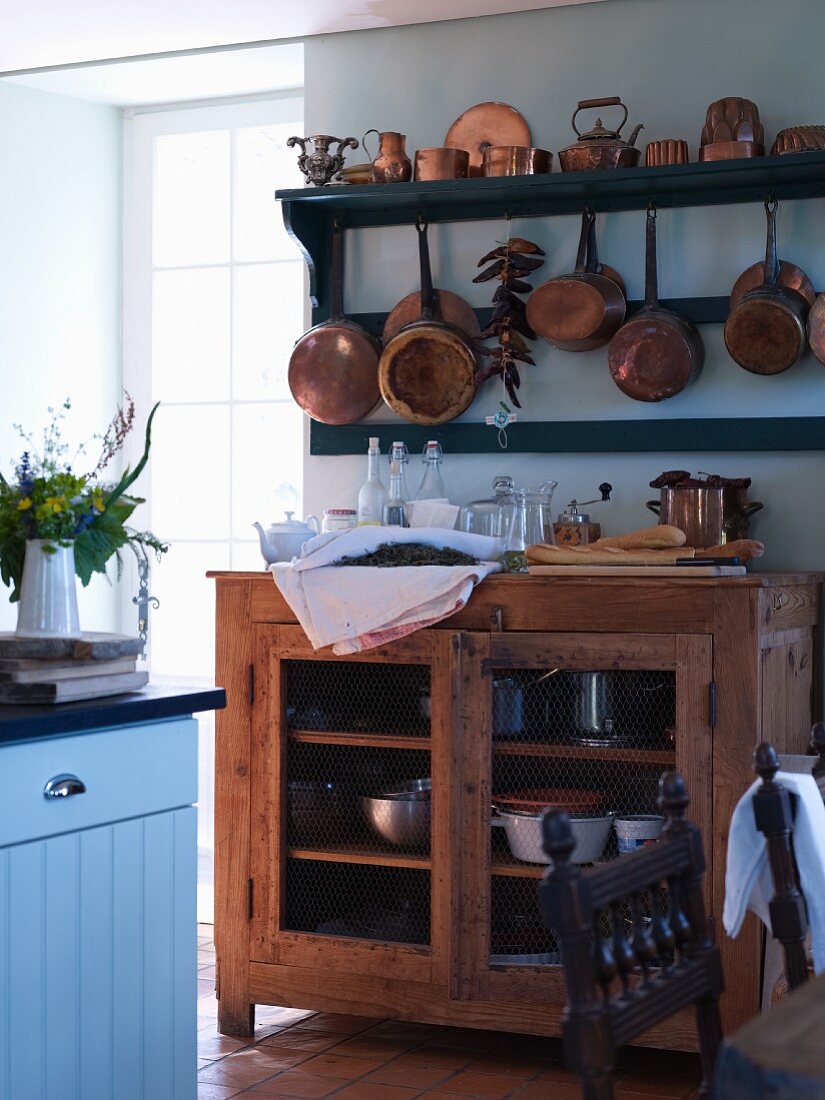 Copper pans on shelves above open-fronted wooden cabinet