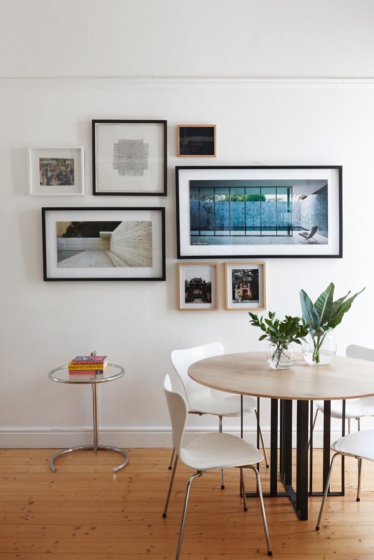 Runder Tisch mit Designerstühlen vor Wand mit Bildergalerie