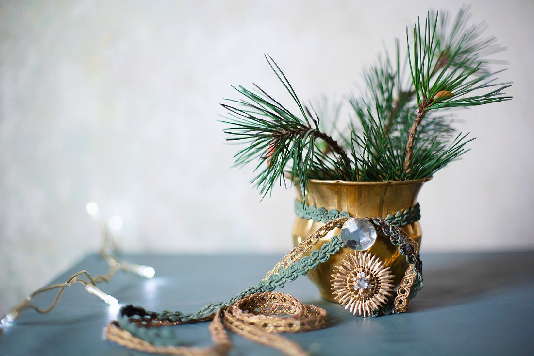 Brocade ribbons tied around gilt vase of fir branches