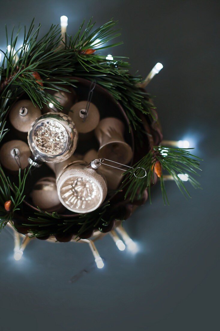 Christmas-tree baubles in dish with fir branches and fairy lights