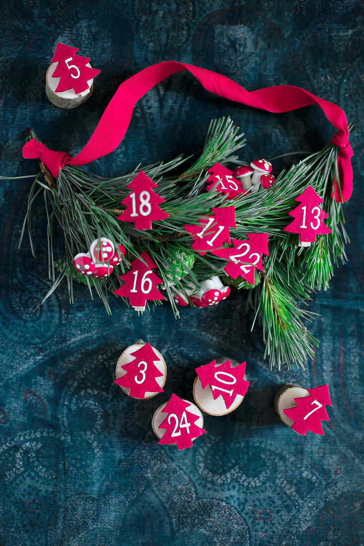 Small, numbered, felt trees arranged on wooden discs next to pine twigs