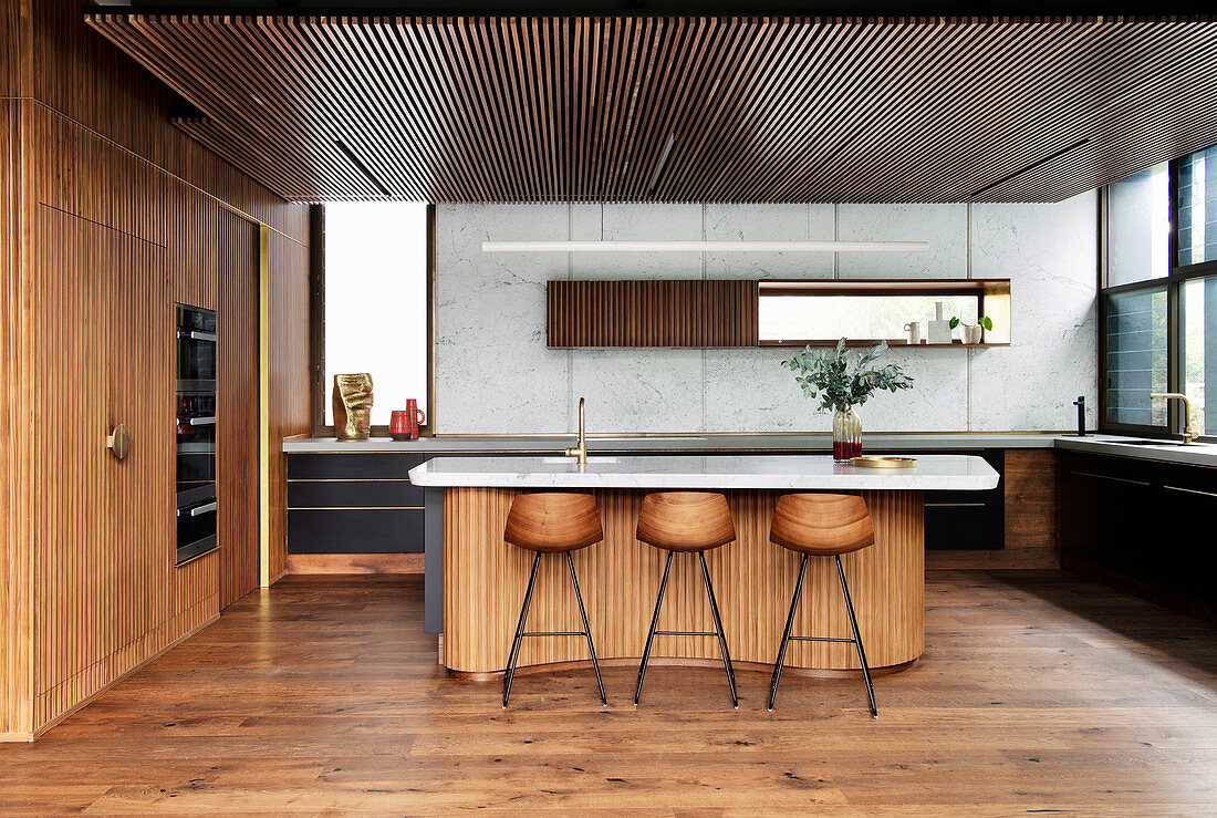 Kitchen island with marble top and bar stools in an open kitchen with wooden paneling