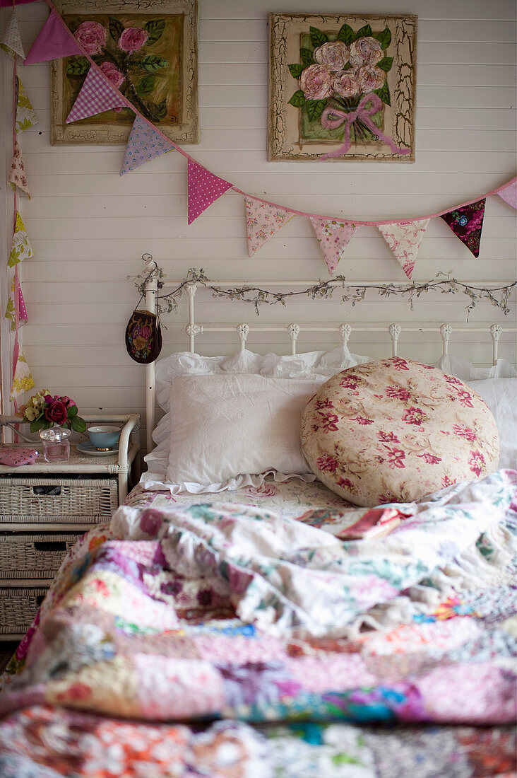 Vintage Bett mit bunter, nostalgischer Bettwäsche, daneben Rattan-Nachttisch und Wimpelkette an der Wand