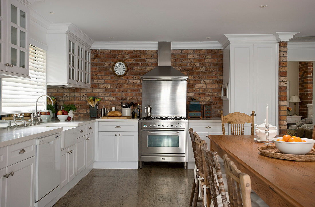 Kitchen with white cabinets, stainless steel cooker against brick wall and solid wooden dining table