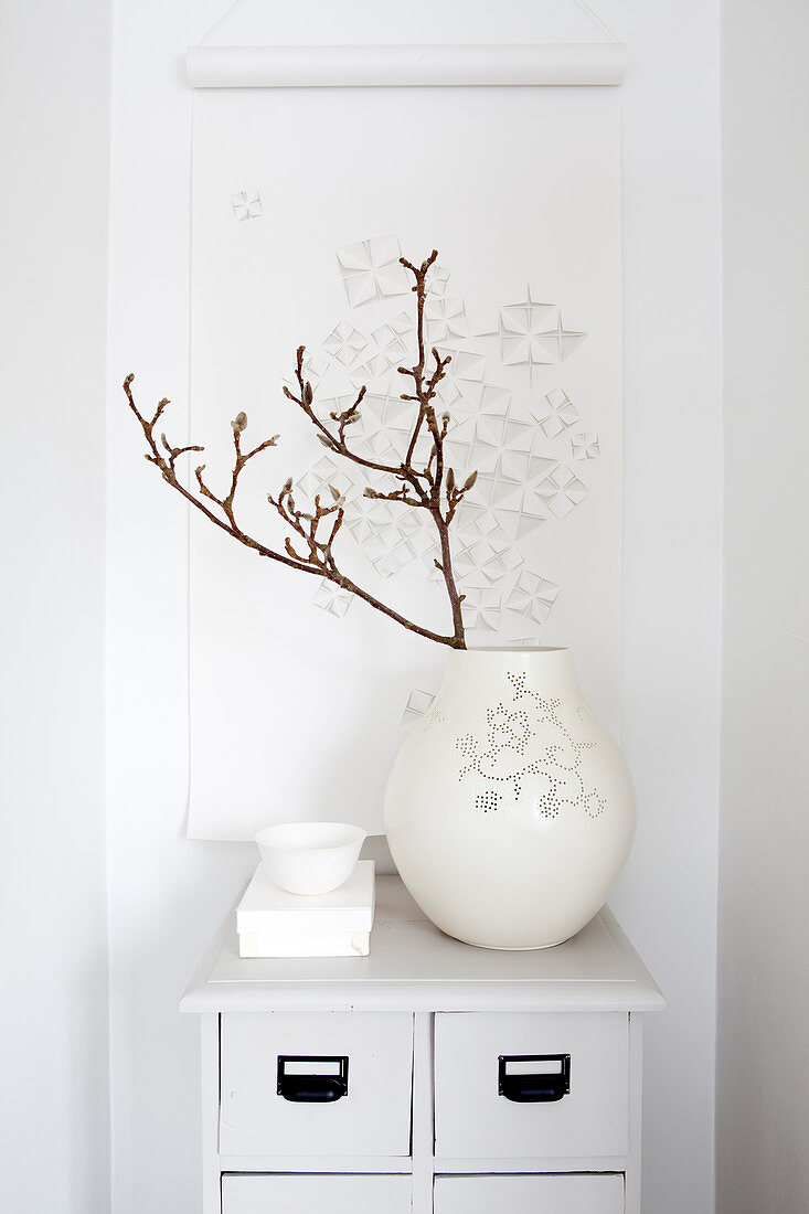 Zweig in weißer Vase vor einer Papierrolle mit Cut Outs