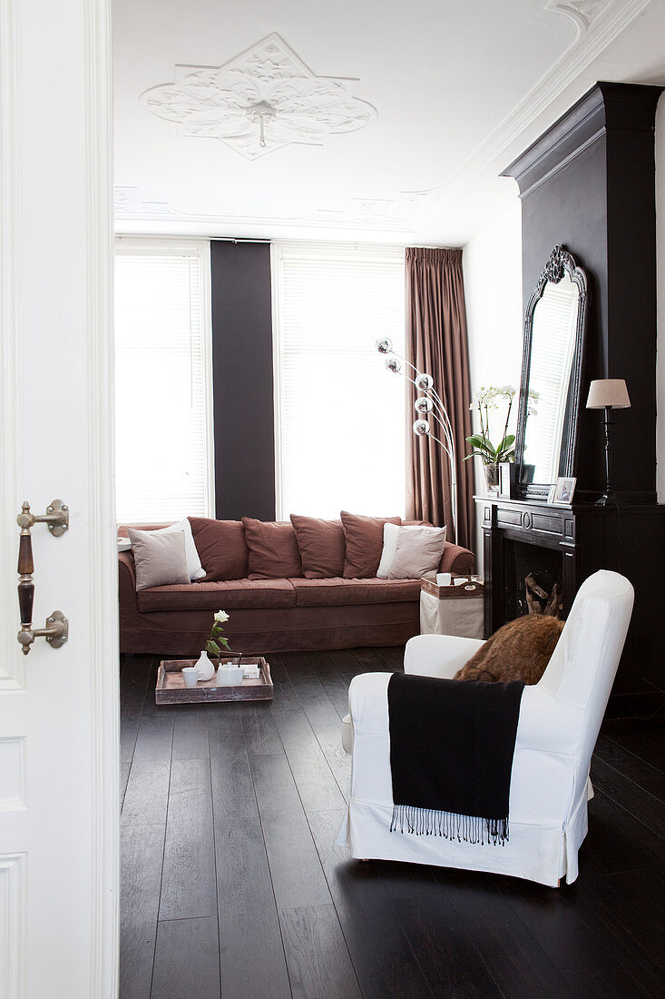 Brown sofa with scatter cushions and armchair with white loose cover next to fireplace in living room