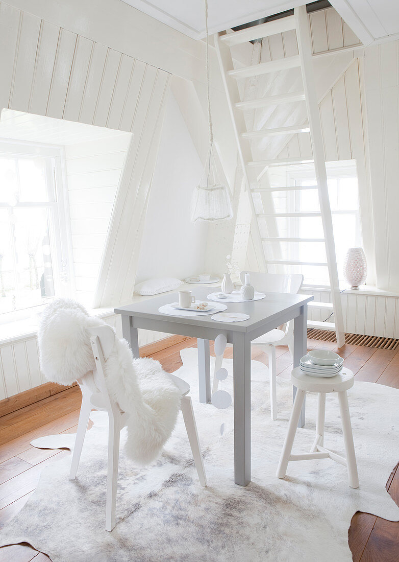 Kleiner Esstisch mit verschiedenen Stühlen in weißem Zimmer mit Gaubenfenster