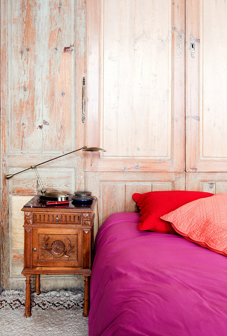 Bett mit Wäsche in Pink und Rot vor einem Wandschrank aus Holz