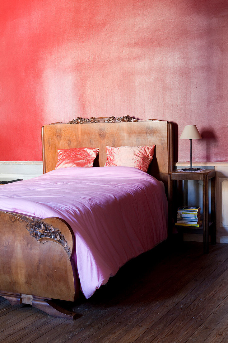Antique bed with carved headboard and foot against pink bedroom wall