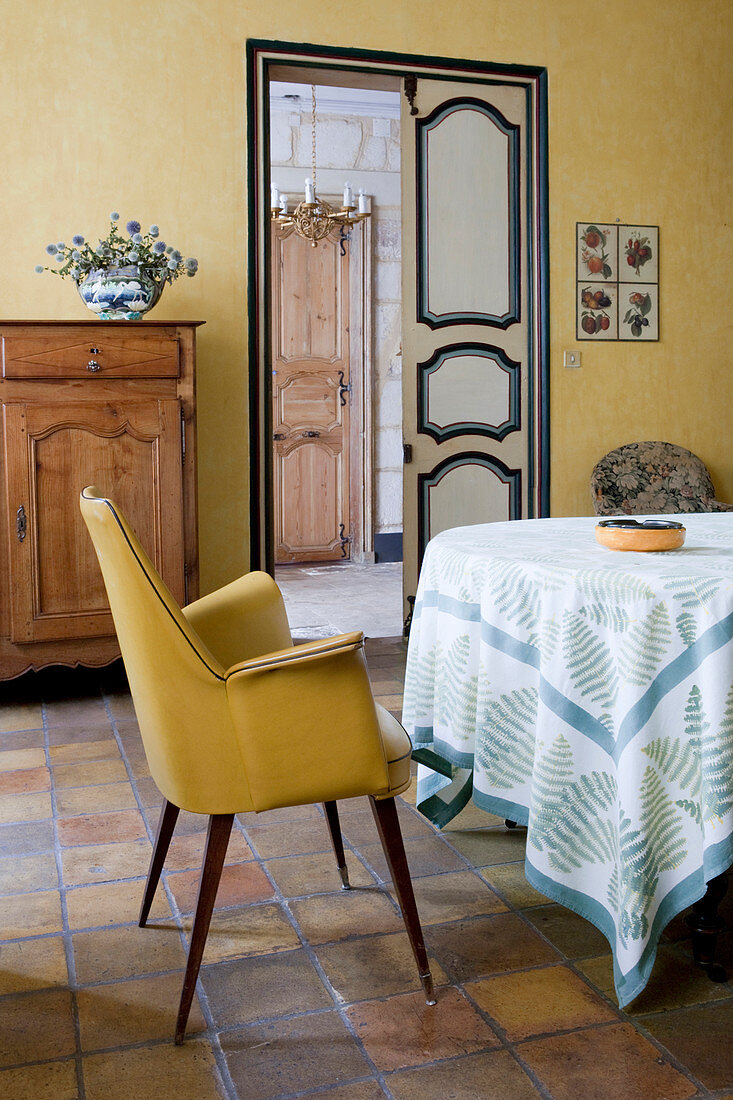 Gelber Polsterstuhl am Tisch im mediterranen Esszimmer mit Terracottafliesenboden