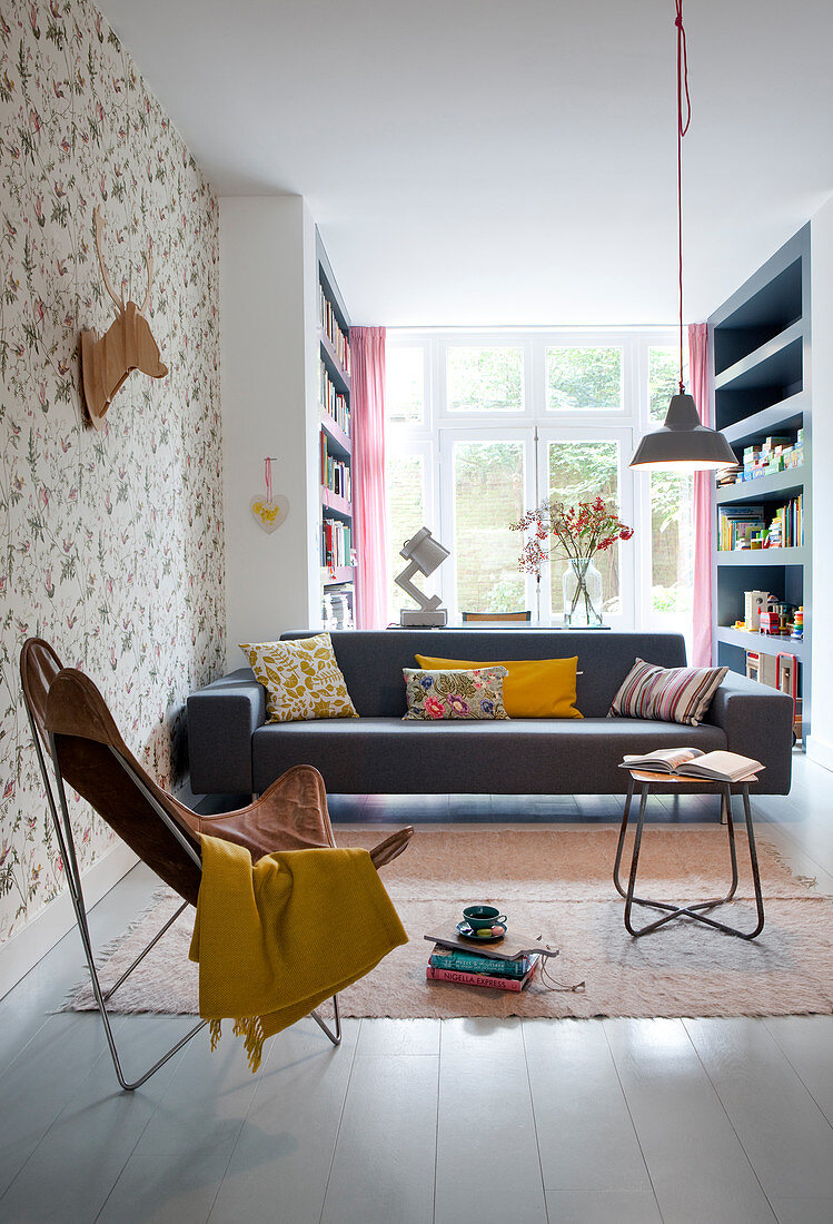 Schwarze Couch, Klassikerstuhl und stilisiertes Geweih an tapezierter Wand