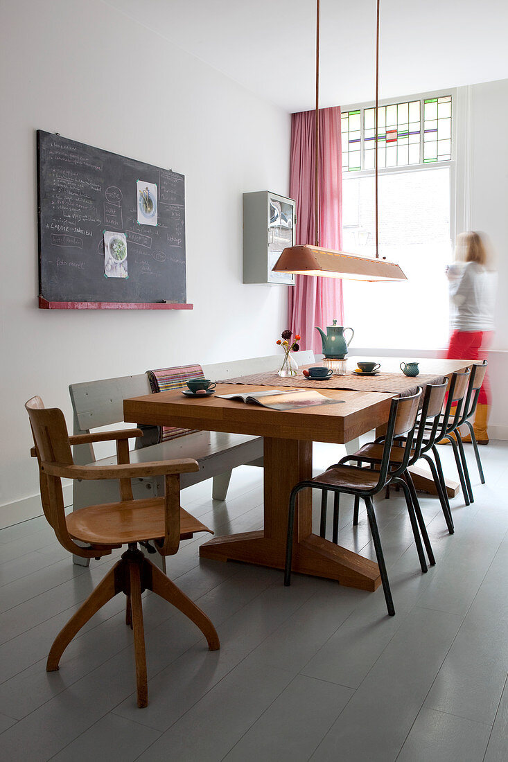 Solid wooden dining table with chairs and bench next to chalkboard on wall