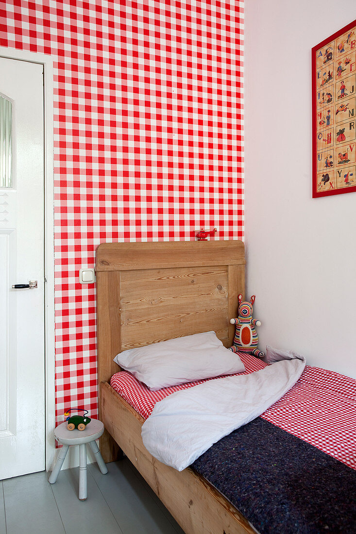 Wooden bed with tall headboard against wall covered in red-and-white gingham wallpaper