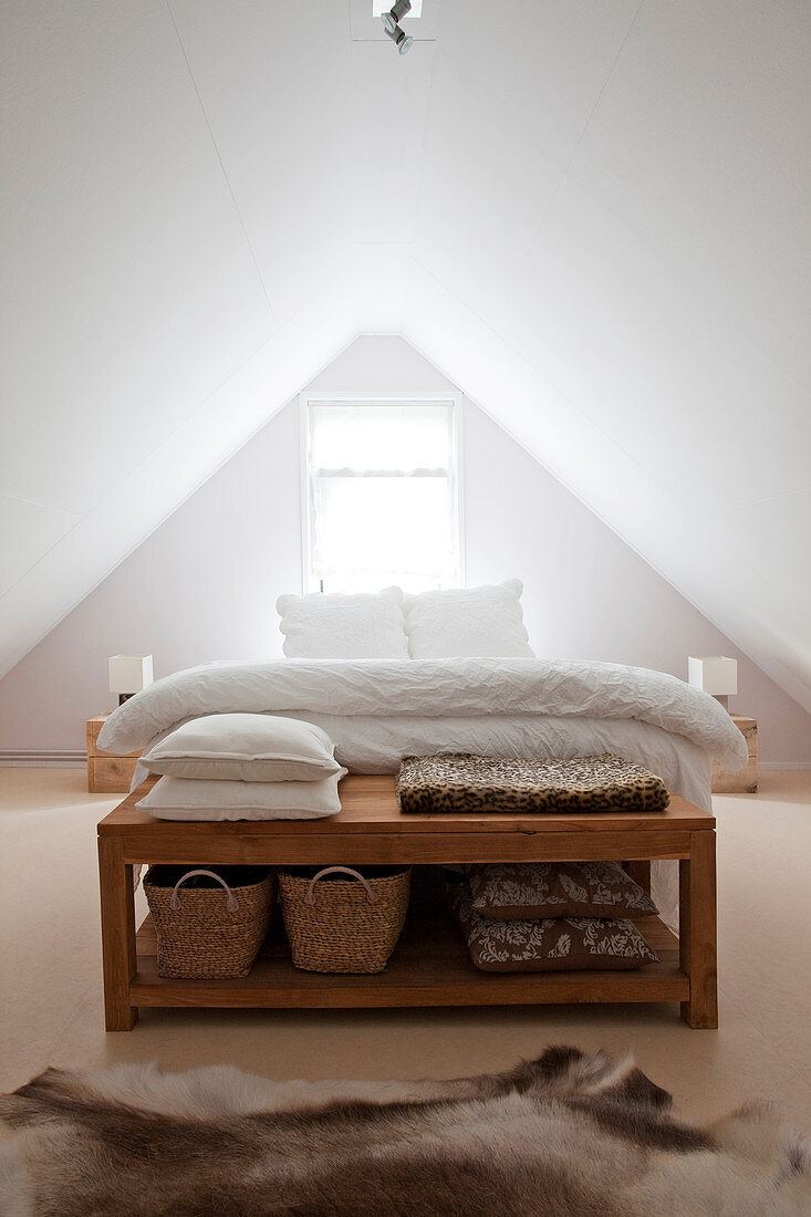 Holzbank am Bettende in weißem Schlafzimmer im Dachgeschoss