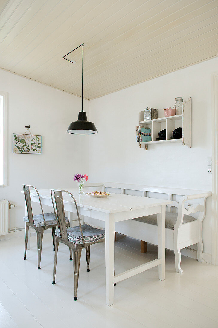 Metal chairs and bench around a wooden table in a white dining room