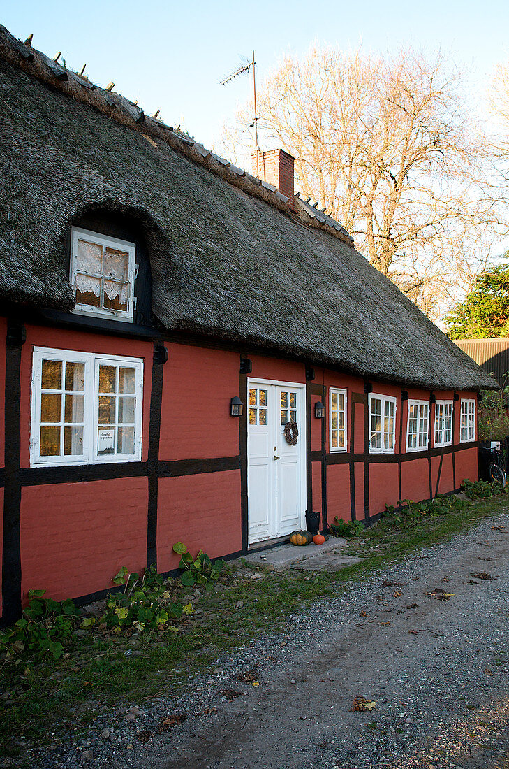 Red half-timbered house with thatched roof on the gravel path in autumn