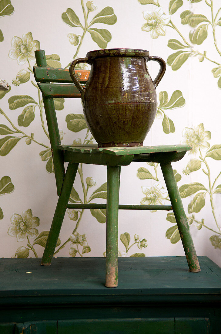 Tonkrug auf grünem alten Kinderstuhl vor Tapete mit floralem Motiv