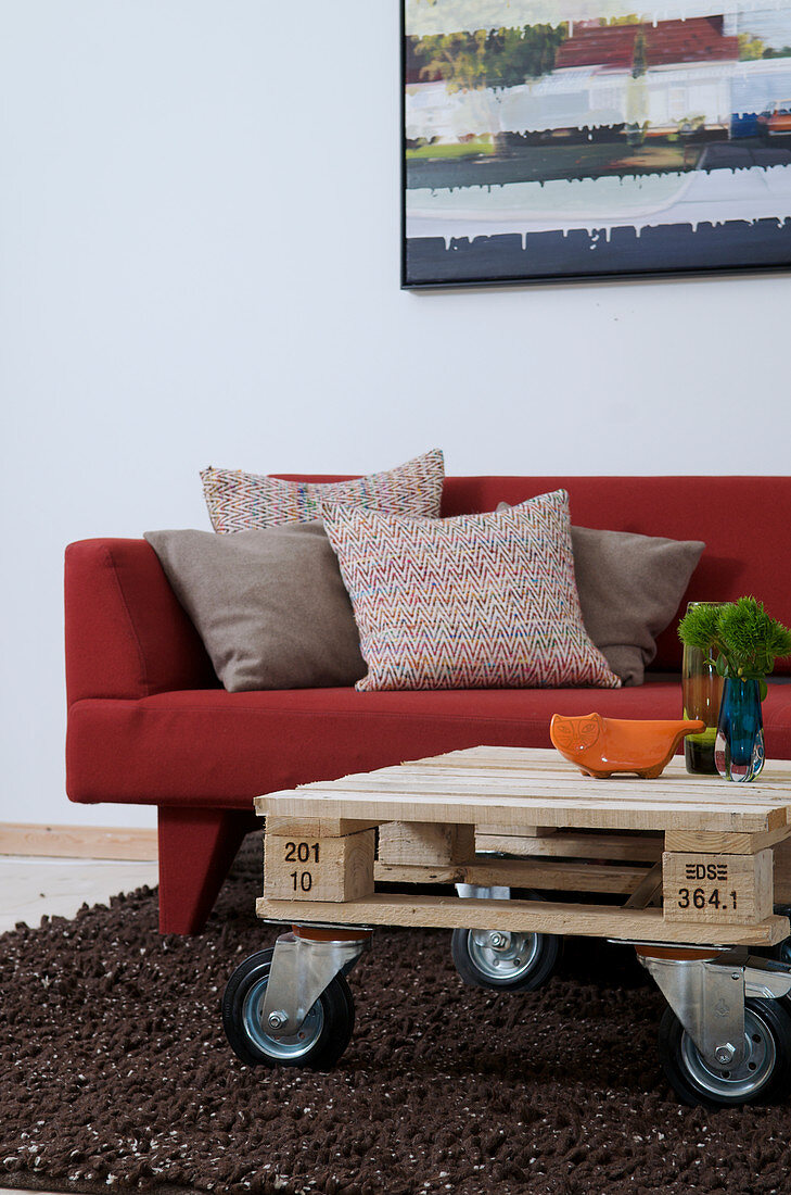 Palette auf Möbelrollen als Couchtisch vorm roten Sofa