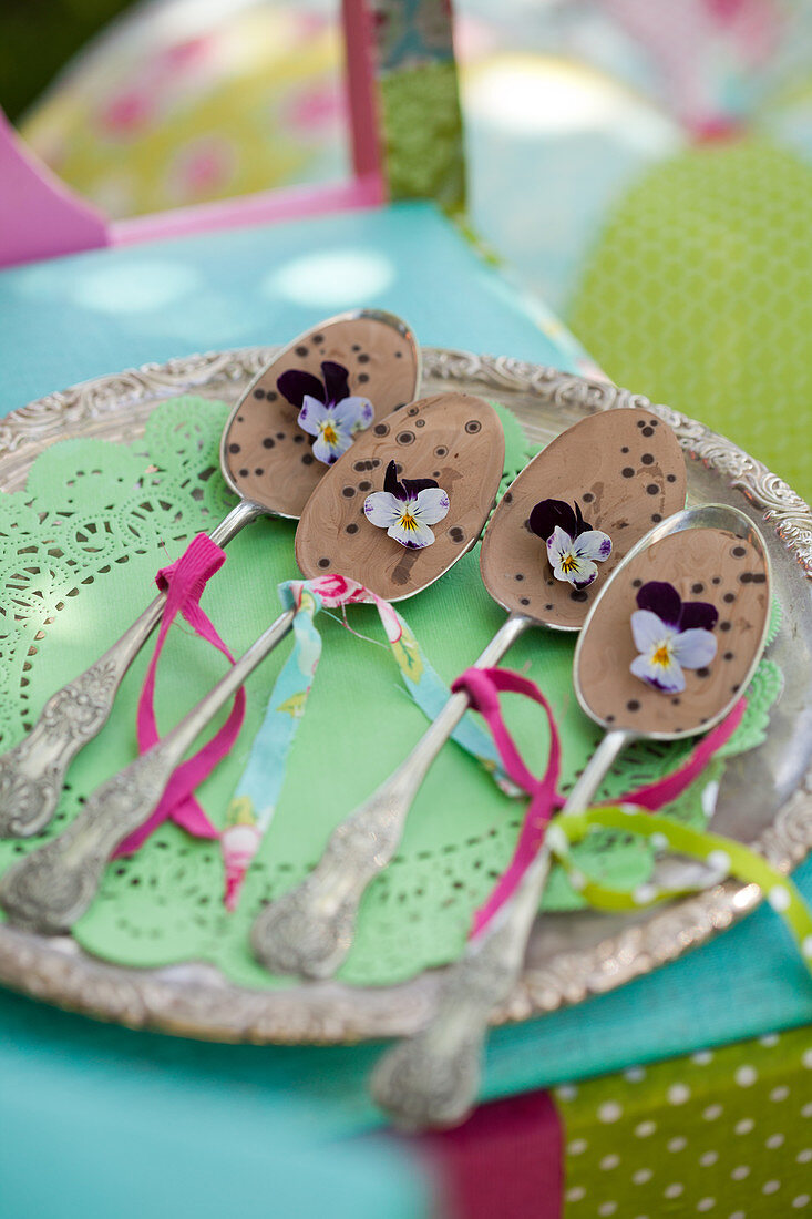 Silver spoons filled with chocolate and decorated with ribbons and violas