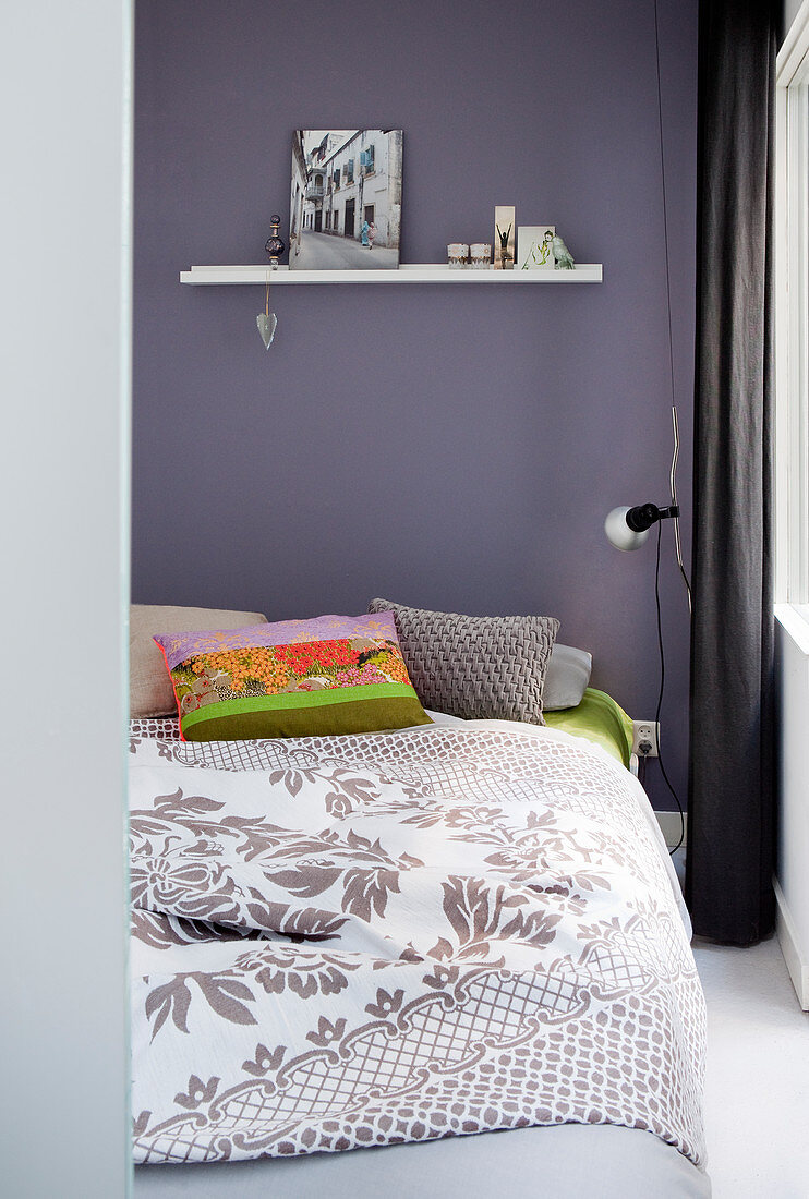 Doppelbett mit Tagesdecke und bunten Kissen im Schlafzimmer vor dunkler Wand