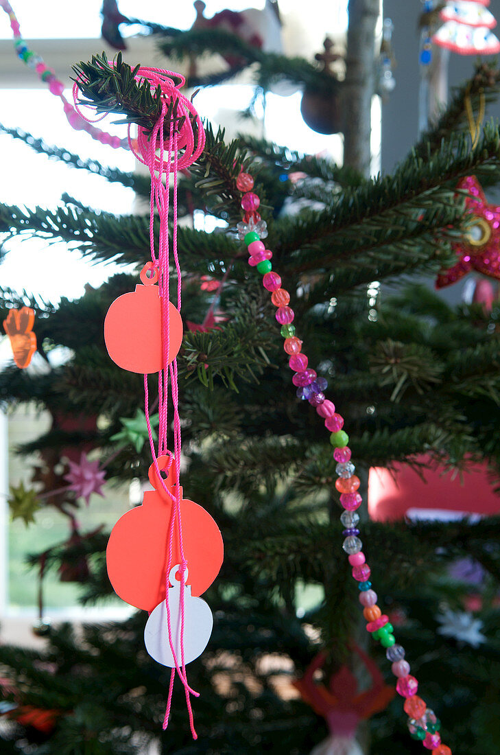 Paper silhouettes of Christmas-tree baubles and colourful string of beads on Christmas tree