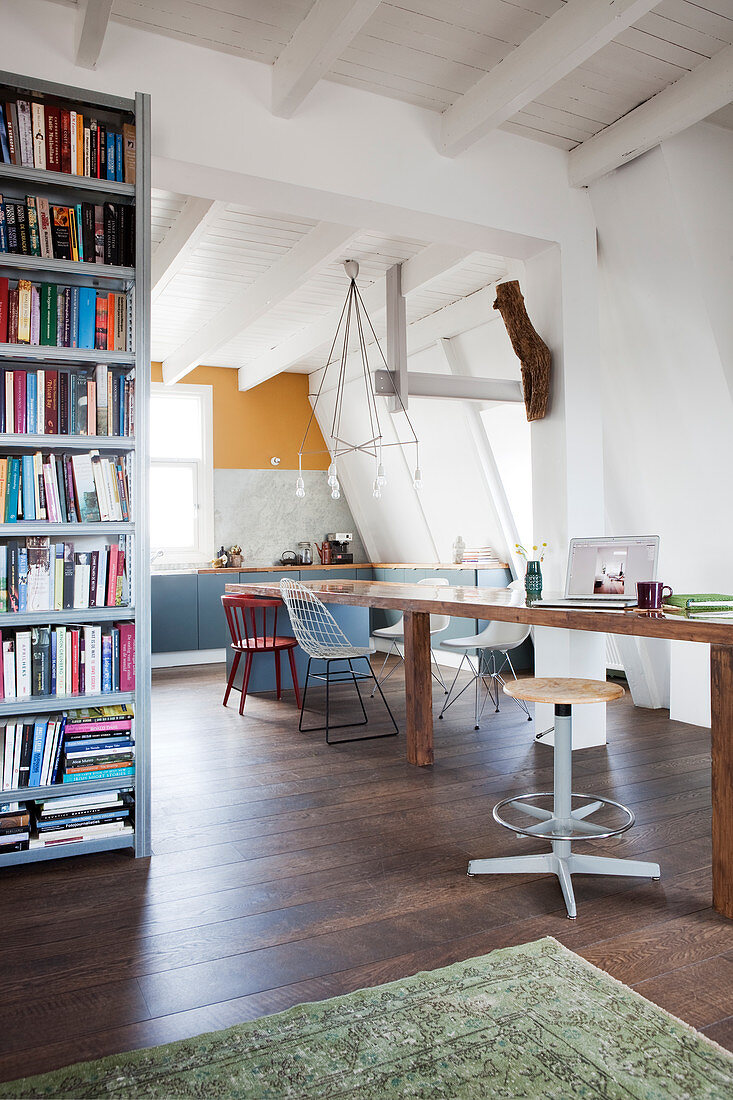 Langer Esstisch mit verschiedenen Stühlen und Bücherregal in offenem Wohnraum