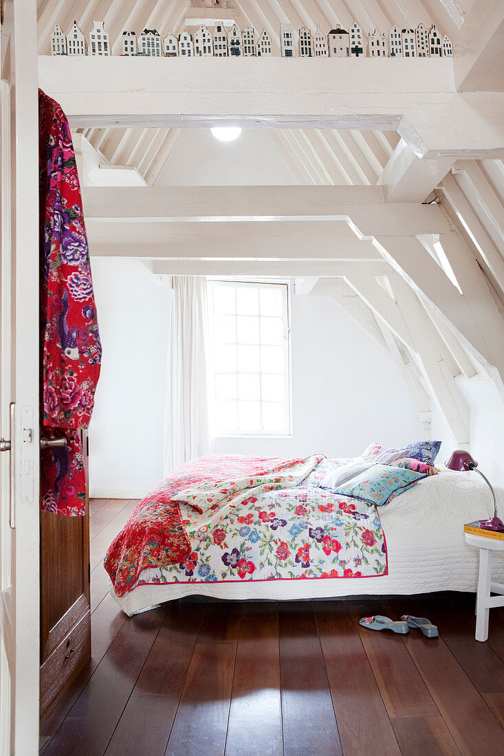 Blick ins weiße Dachgeschosszimmer auf Doppelbett mit bunten Kissen und Steppdecke