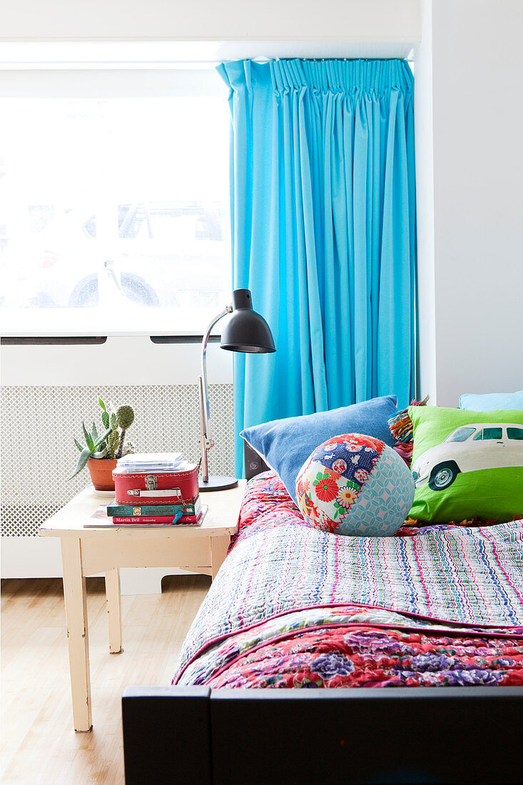 Bett mit bunten Decken und Nachttisch im Jungenzimmer mit türkisblauem Vorhang