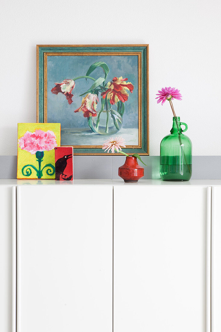Flowers and pictures on top of tall white sideboard