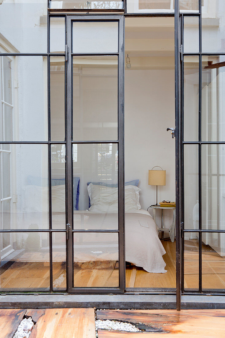 Blick durch Industrieverglasung auf Doppelbett im Schlafzimmer
