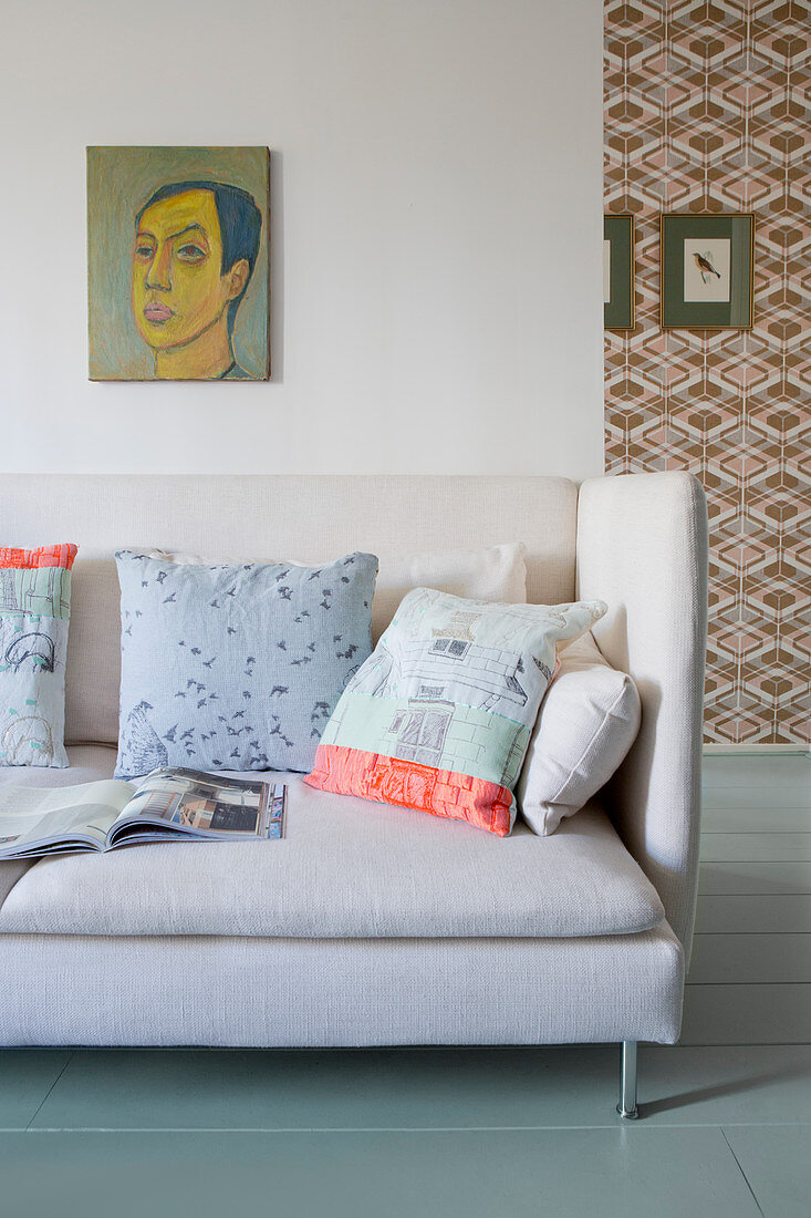 Scatter cushions on pale sofa below portrait on wall