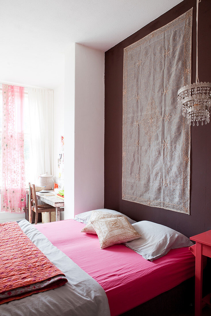 Matratze mit pinkfarbenem Spanntuch vor dunkler Wand mit Wandbehang im Schlafzimmer
