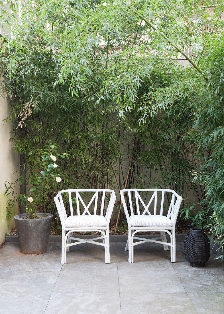 Zwei weiße Stühle auf bewachsener Terrasse mit Fliesenboden
